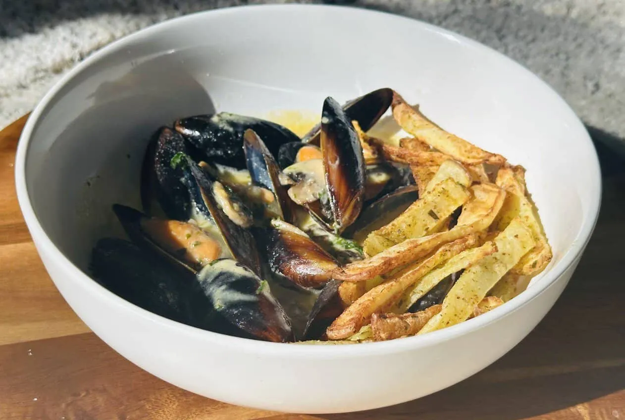 Bowl of mussels in creamy sauce with crispy fries on a wooden table. Perfect seafood dish for a tasty meal.